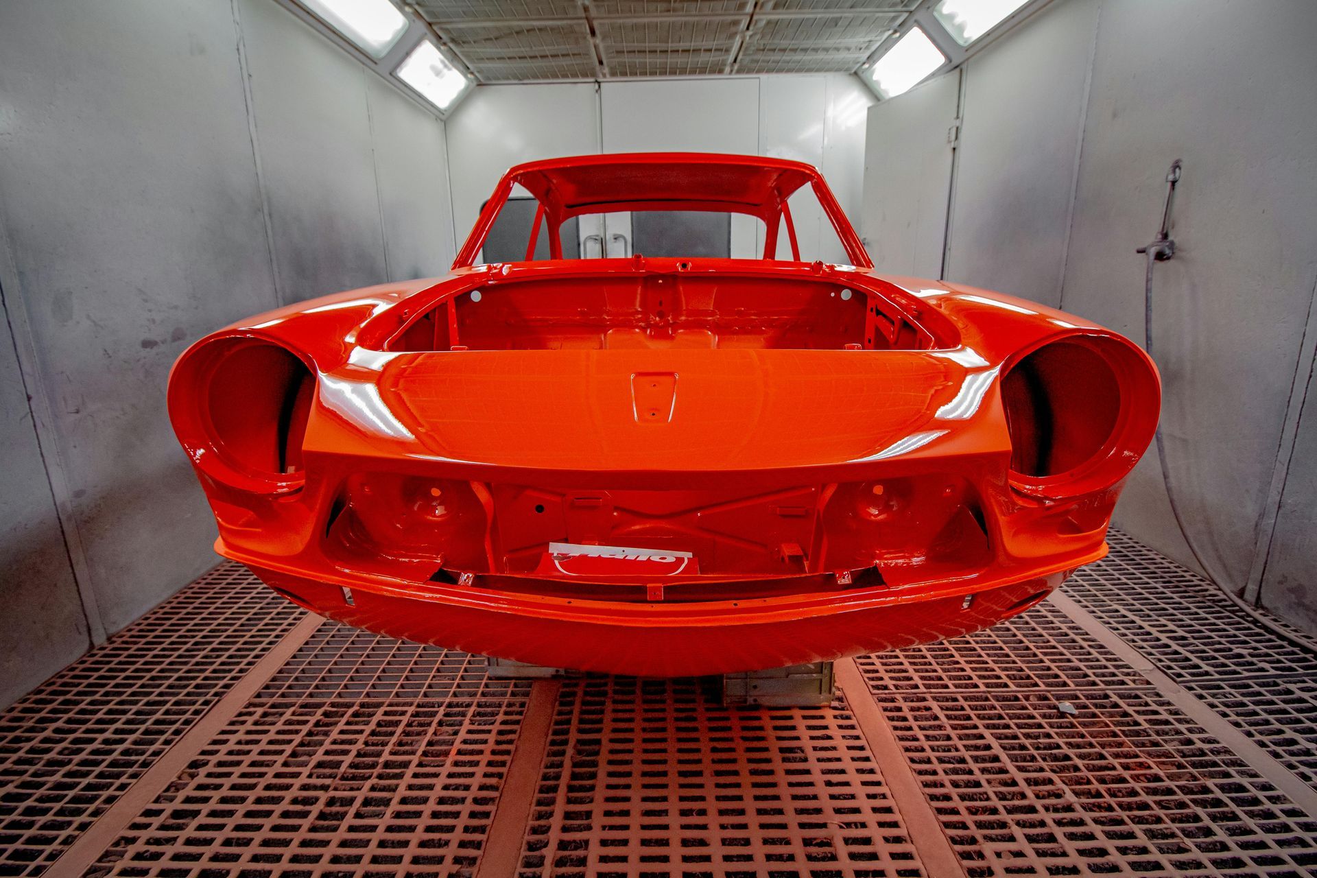An orange car is sitting in a paint booth.