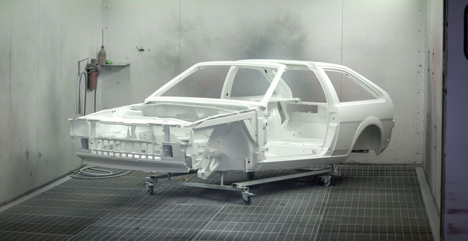 A white car is being painted in a paint booth