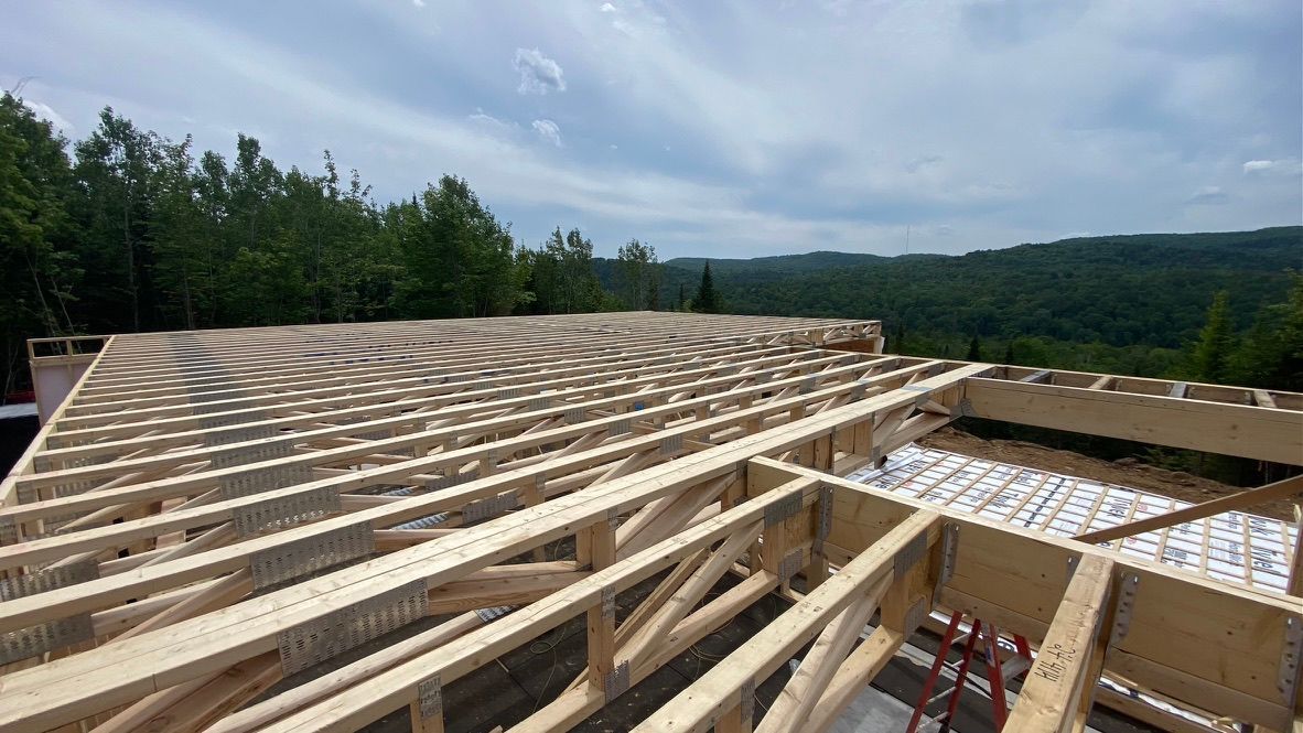 Des fermes de toit en bois sont installées sur la charpente d'une maison, avec un paysage forestier en arrière-plan.