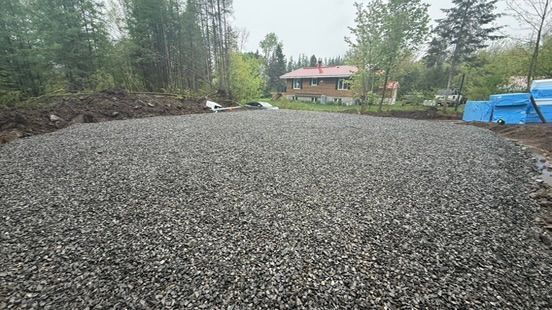 Zone recouverte de gravier ; terrain préparé pour la construction, avec une maison visible en arrière-plan.