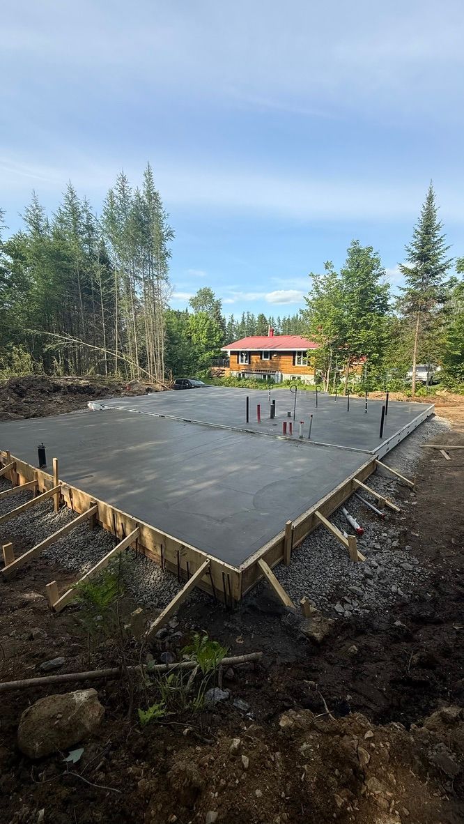 Fondations en béton fraîchement coulé avec ossature en bois, situées dans une zone boisée extérieure.