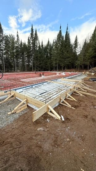 Chantier de construction : coffrages en bois, armatures et préparation du gravier pour une fondation en béton.