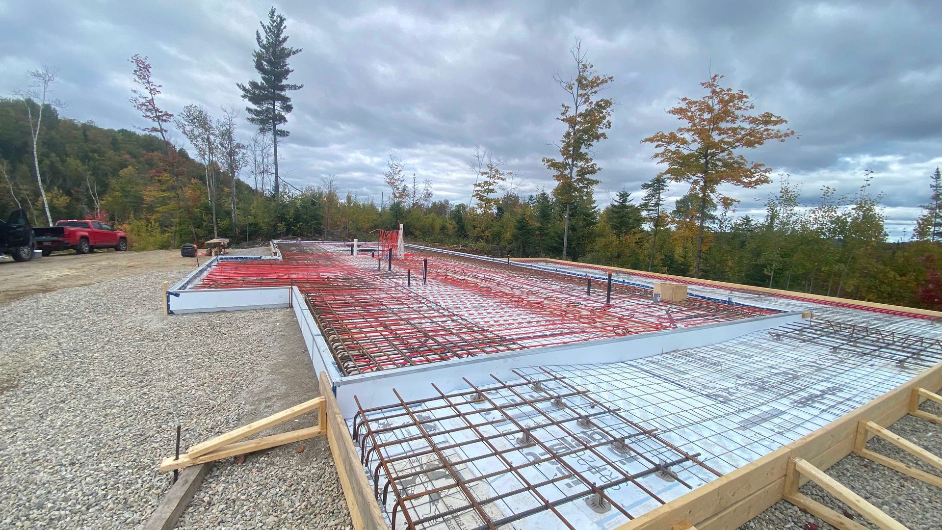 Chantier : Fondations avec tubes de chauffage radiant rouges, armatures et coffrages en bois.
