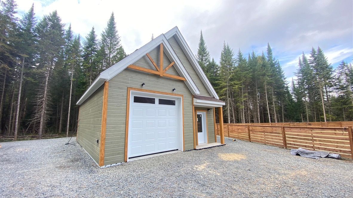 Un petit garage aux murs verts, avec une porte blanche et des boiseries, situé dans une zone gravillonnée.