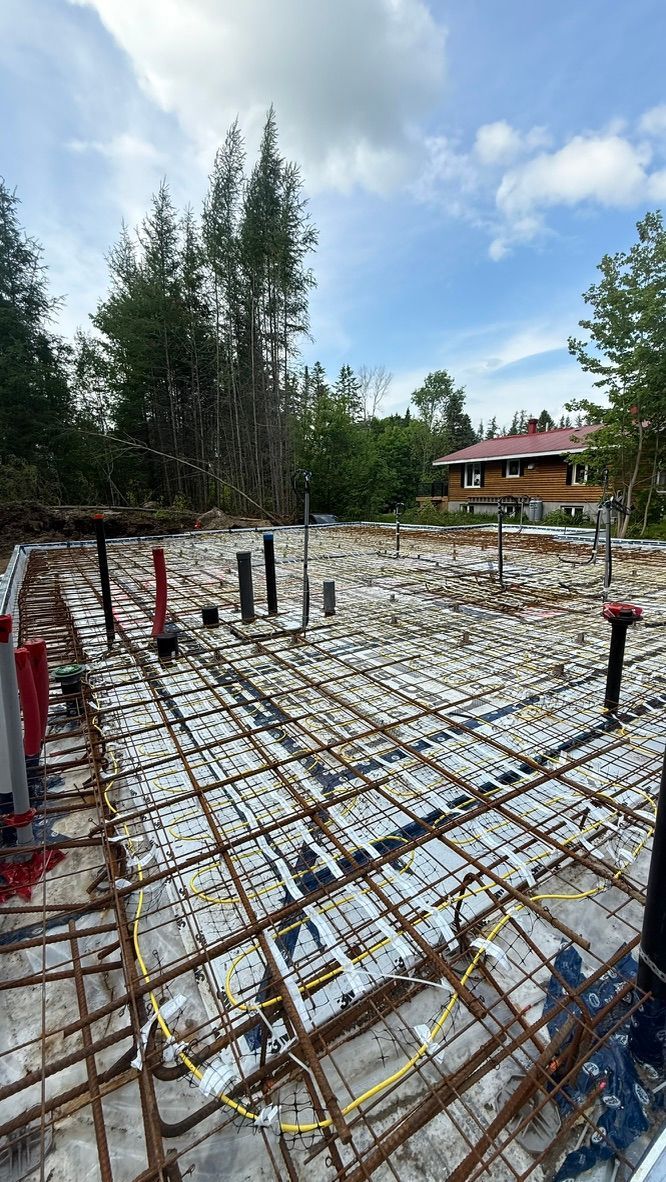 Chantier de construction, treillis d'armature, tuyaux et conduits, dalle de béton partiellement coulée.