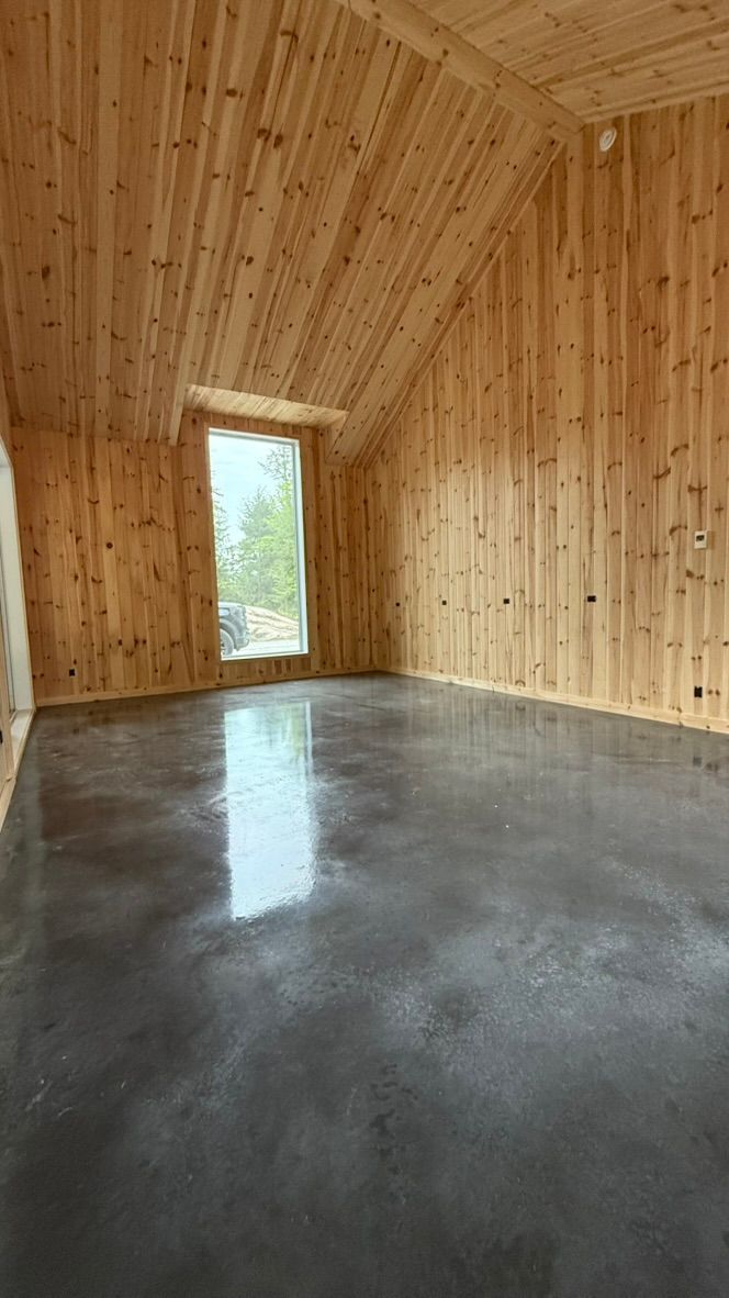 Pièce vide avec murs et plafond en bois, sol en béton gris et fenêtre.