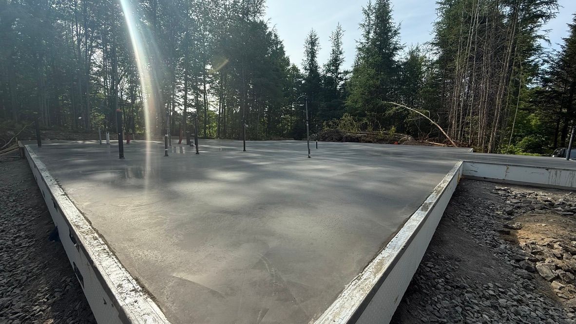 Fondations en béton fraîchement coulé avec armature, entourées de gravier, dans une zone boisée.