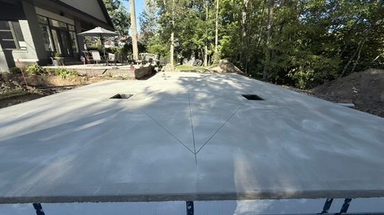 Dalle de béton fissurée, avec deux ouvertures, adossée à une maison et à des arbres.