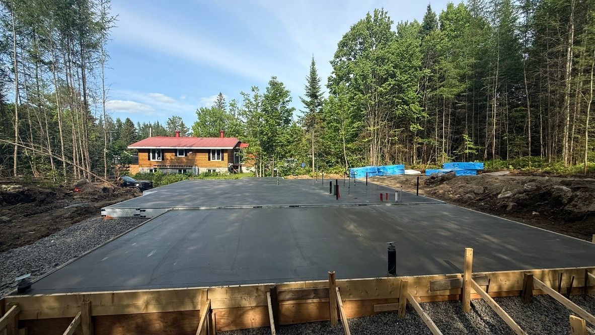 Fondations en béton d'une maison en construction, entourées de forêt.