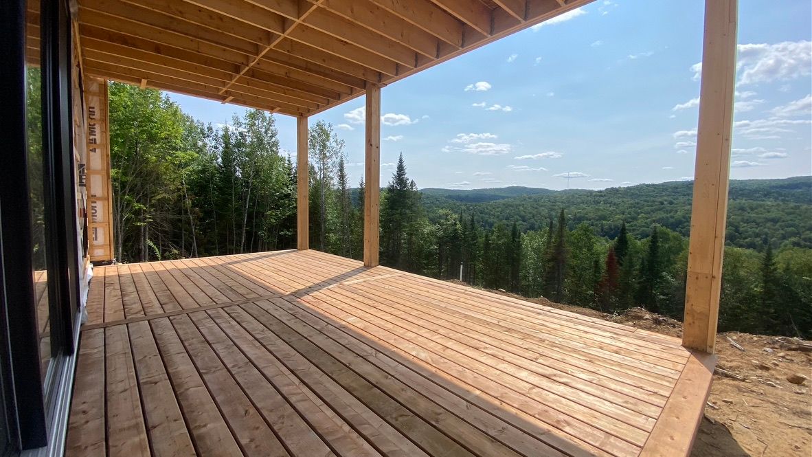 Terrasse en bois en construction donnant sur une forêt verdoyante et un ciel bleu.