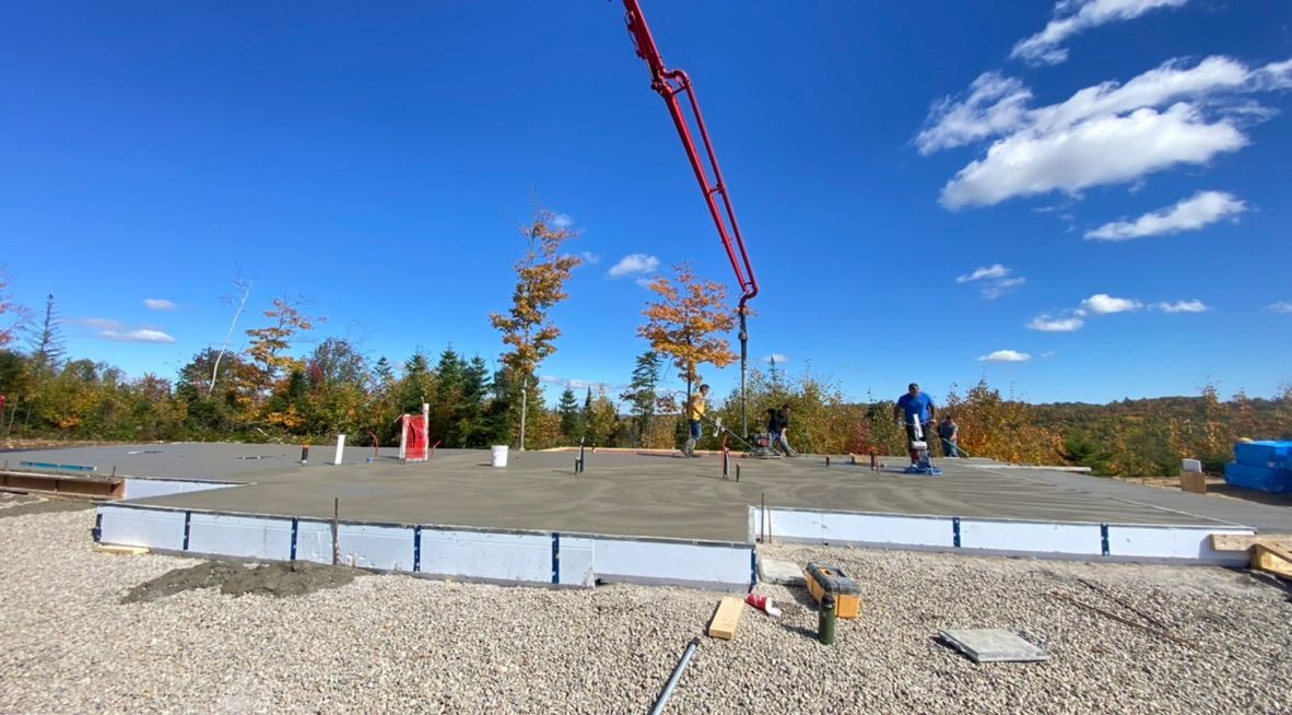 Des fondations en béton sont coulées sur une base de gravier, avec un ciel bleu en arrière-plan.