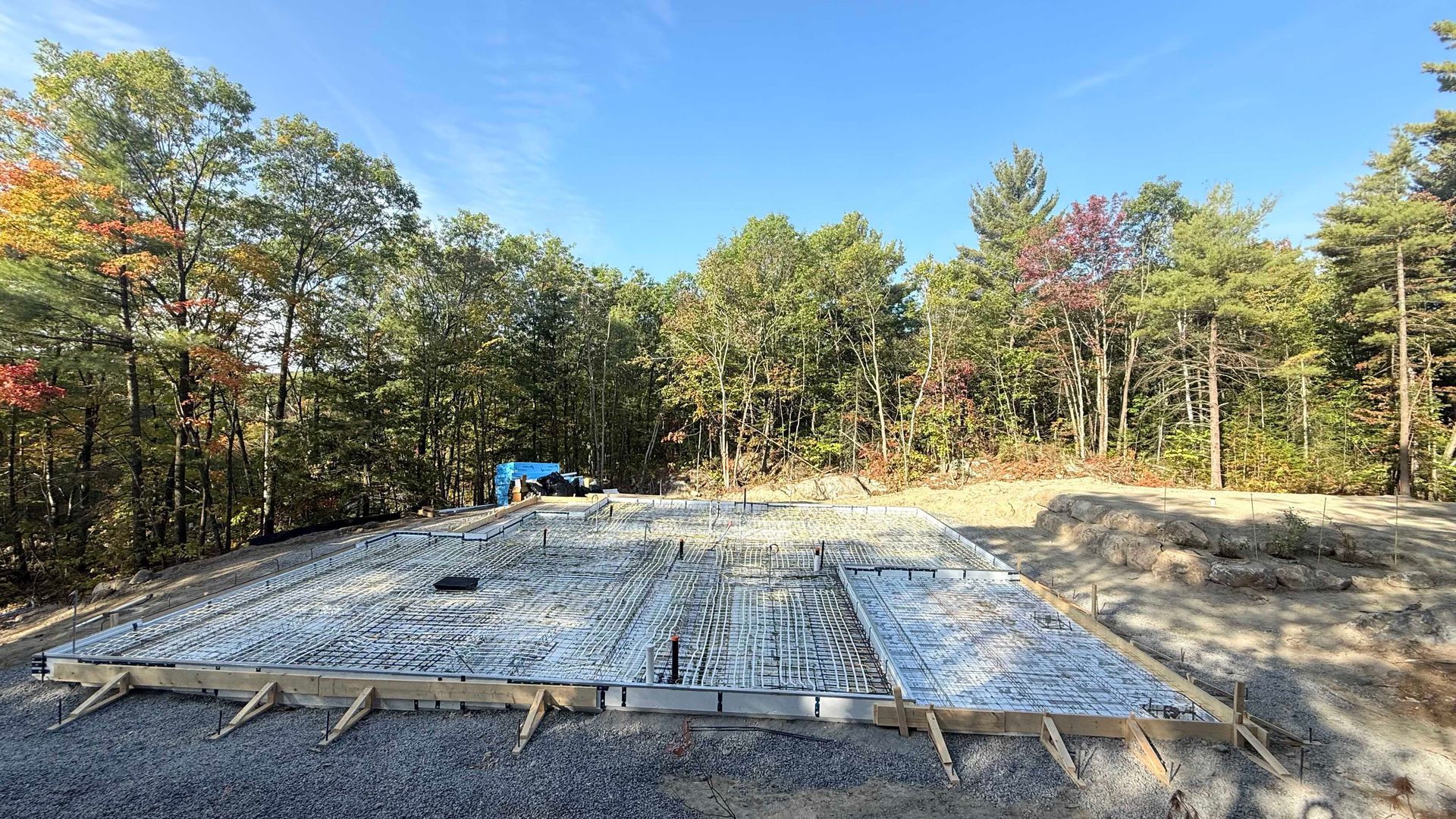 Chantier de construction de fondations avec treillis d'armature, charpente en bois et arbres environnants.