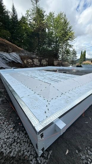 Fondations préfabriquées blanches avec garniture métallique, sur une surface de gravier, adossée à une colline.