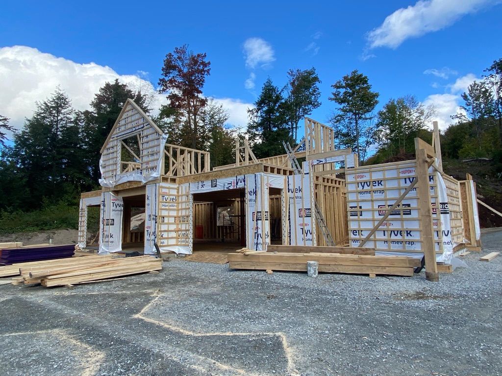 Chantier de construction avec une maison à ossature bois, recouverte de bâche blanche, sur fond de ciel bleu.