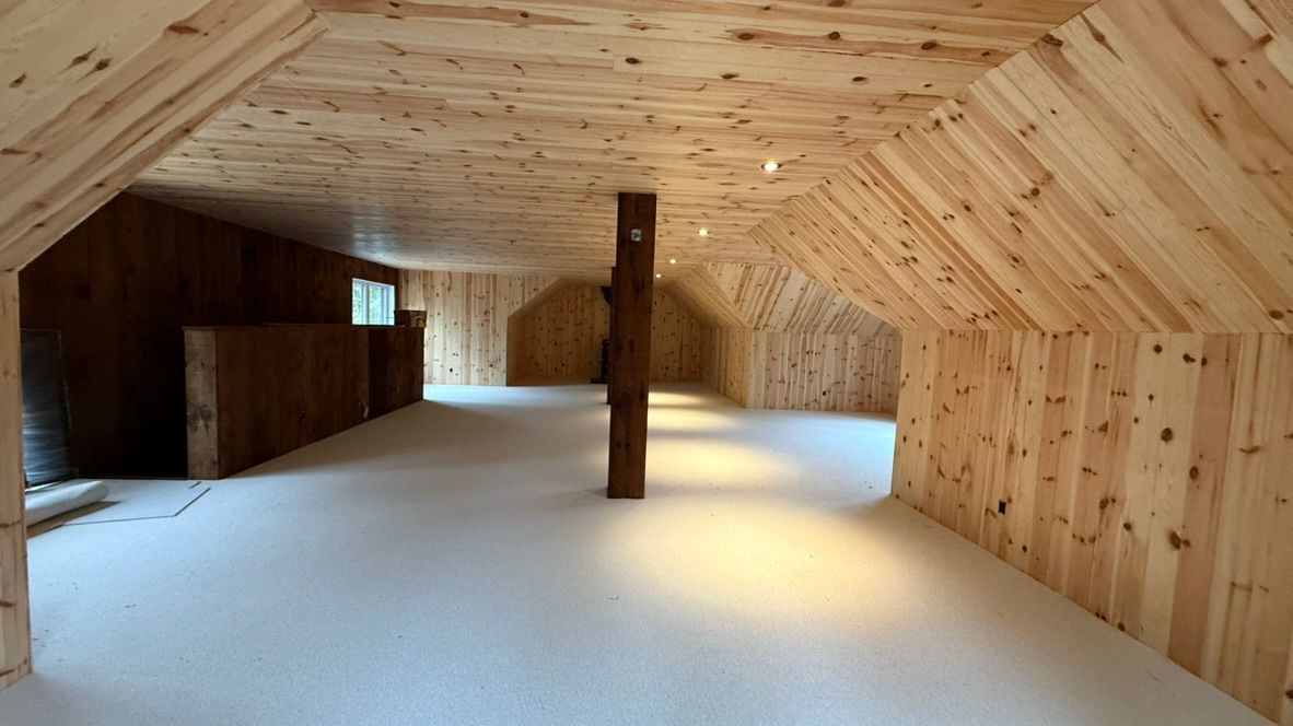 Intérieur d'un grenier avec lambris clair, sol blanc et poutre de soutien centrale.