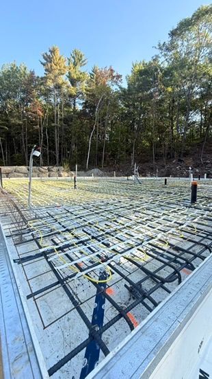 Chantier de construction avec fondations en béton et treillis d'armature, avec des arbres en arrière-plan.