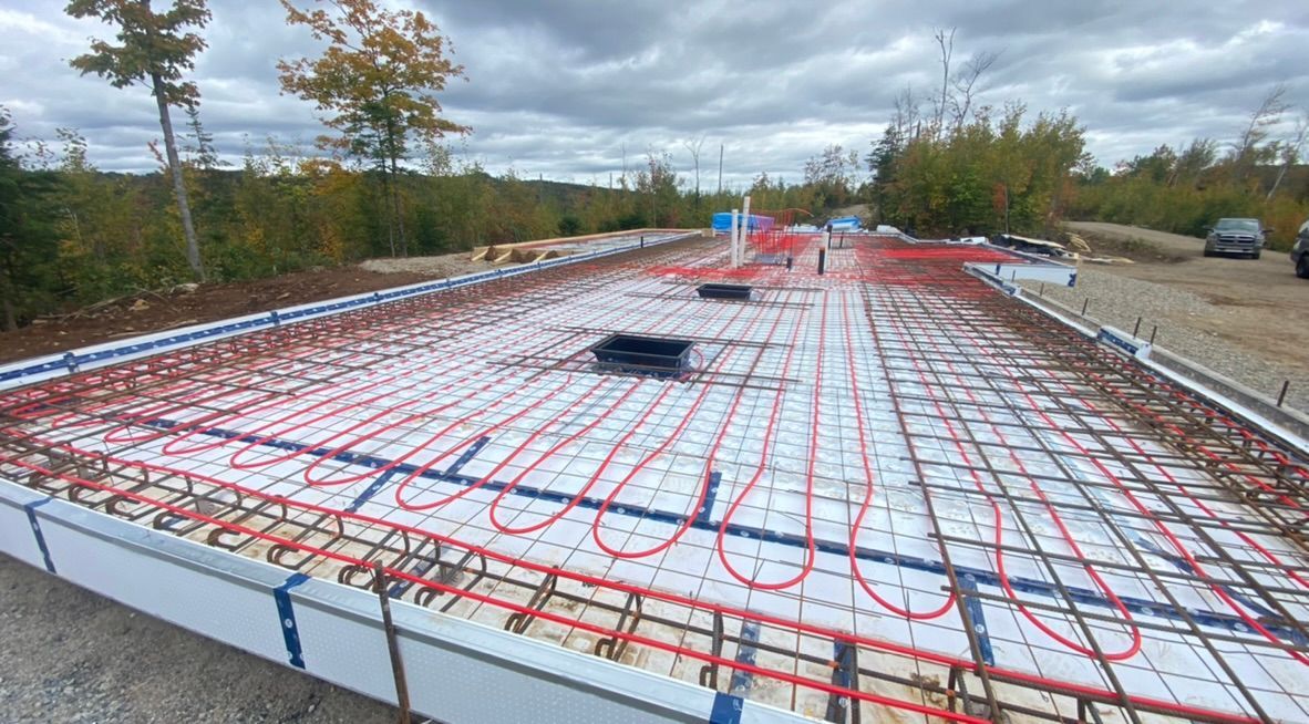 Chantier de construction avec des tuyaux de chauffage au sol radiant rouges et bleus disposés en grille.