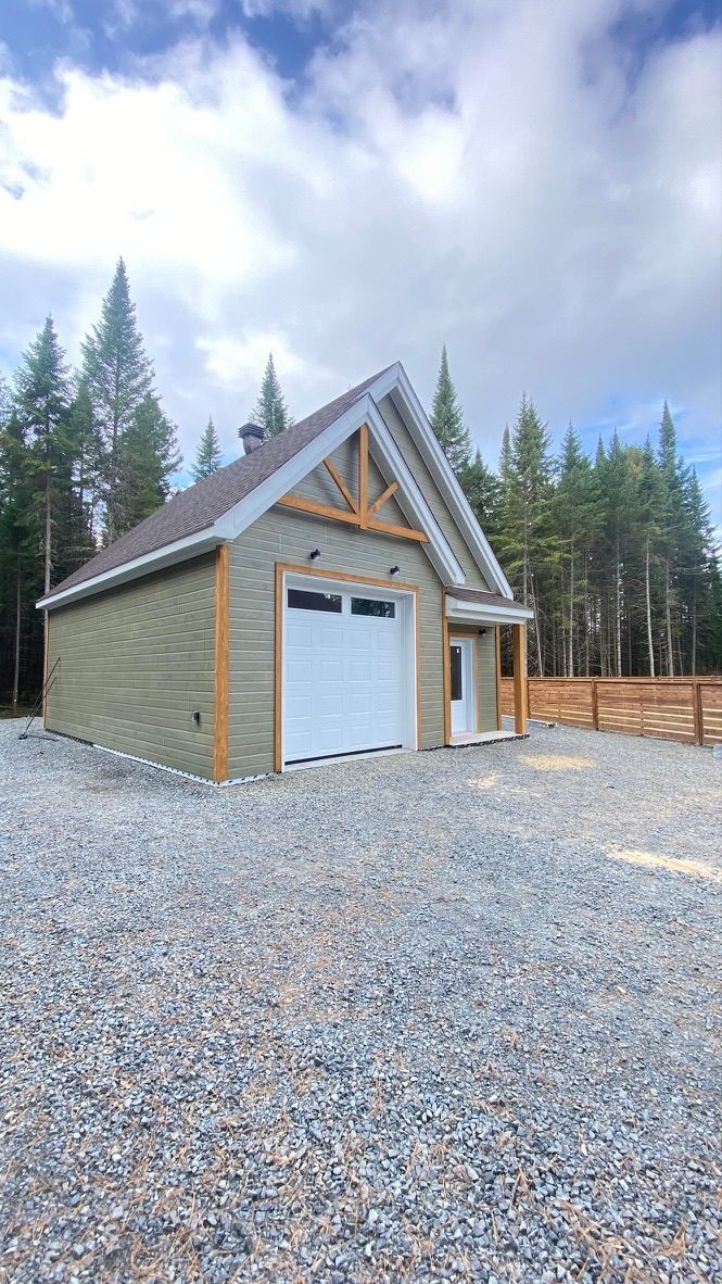 Garage avec bardage vert clair, porte de garage blanche et allée en gravier.