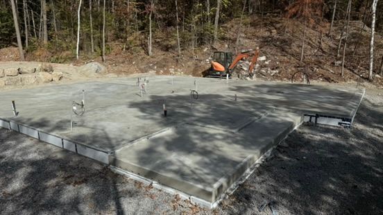 Dalle de fondation en béton avec canalisations intégrées, chantier de construction avec excavatrice en arrière-plan.