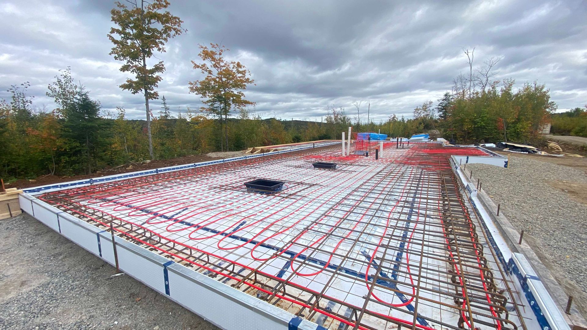 Chantier de construction avec des tuyaux rouges et bleus posés sur une base en mousse blanche, entouré de gravier et d'arbres