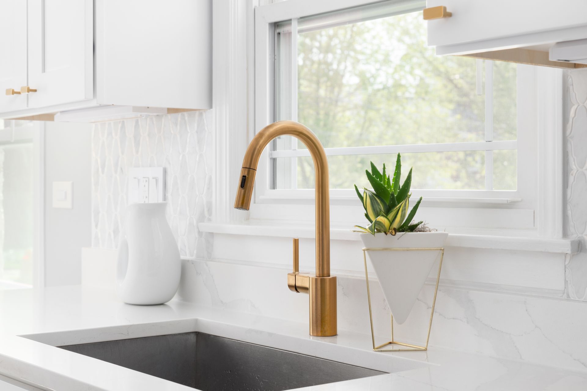 A kitchen sink with a gold faucet and a potted plant on the counter.