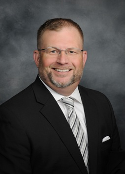 Portrait of a smiling man in a black suit and striped tie against a gray studio backdrop