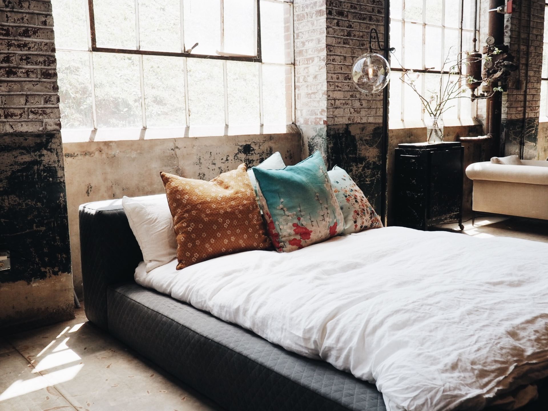 A bed with white sheets and pillows in a room with a brick wall.