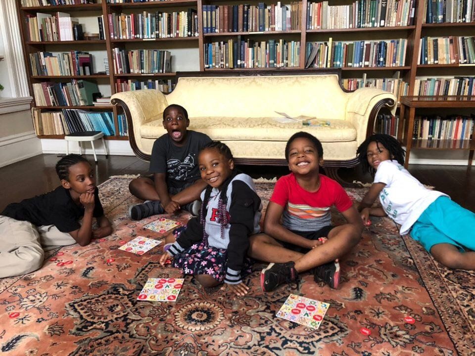 four children sitting on the floor of a library smiling