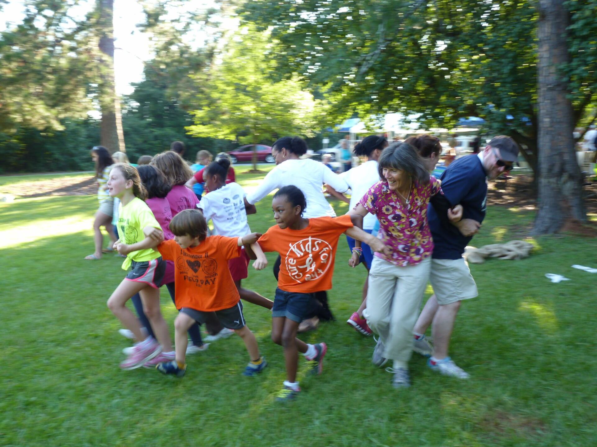 Adults and children with arms connected in a circle facing out playing a game