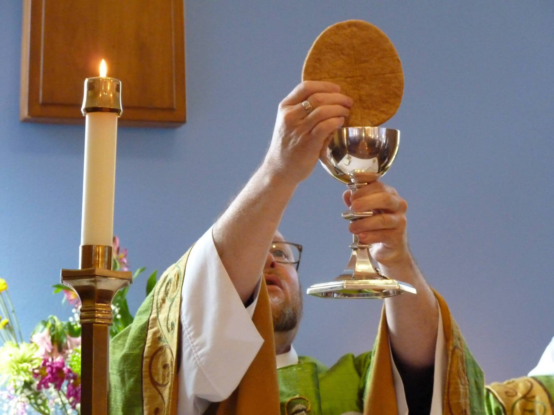 Image of priest holding up communion bread and chalice during worship