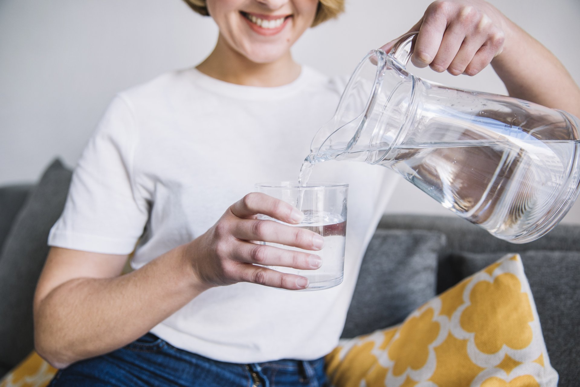 Mulher sorrindo e segurando jarra com água, despejando em um copo