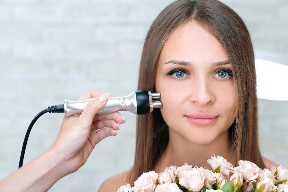 Mulher jovem segurando buquê de flores recebendo tratamento facial por radiofrequência
