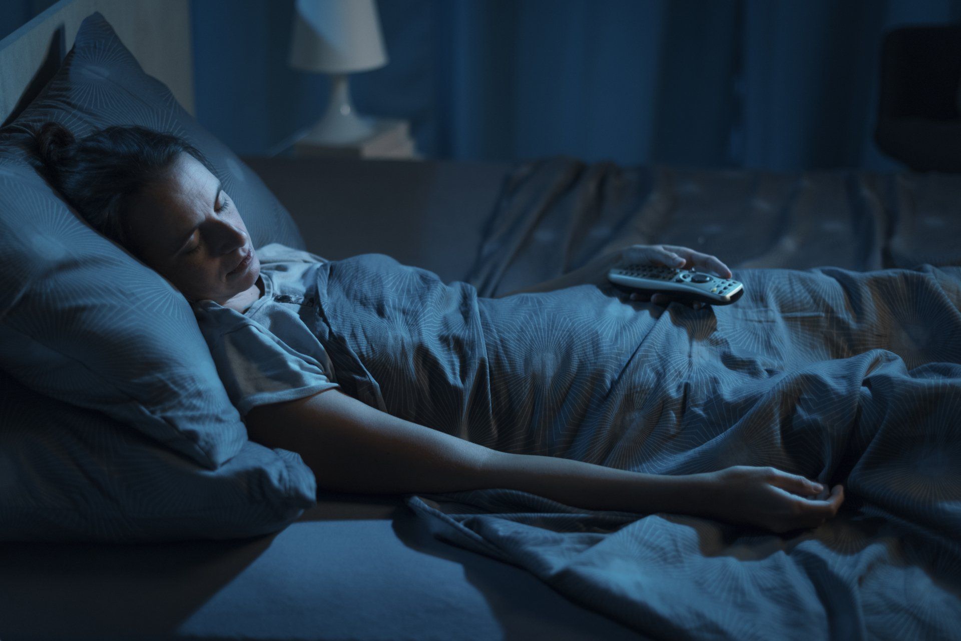 Mulher dormindo com a luz apagada e televisão ligada, com celular no colo