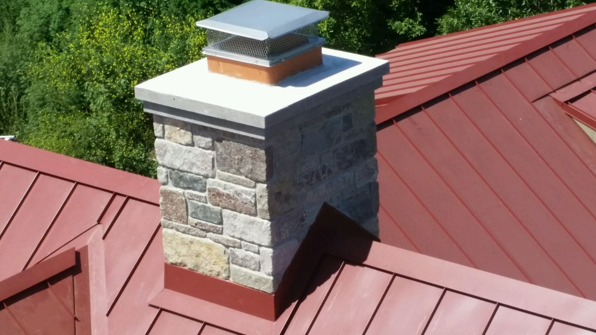 A chimney on top of a red roof with trees in the background