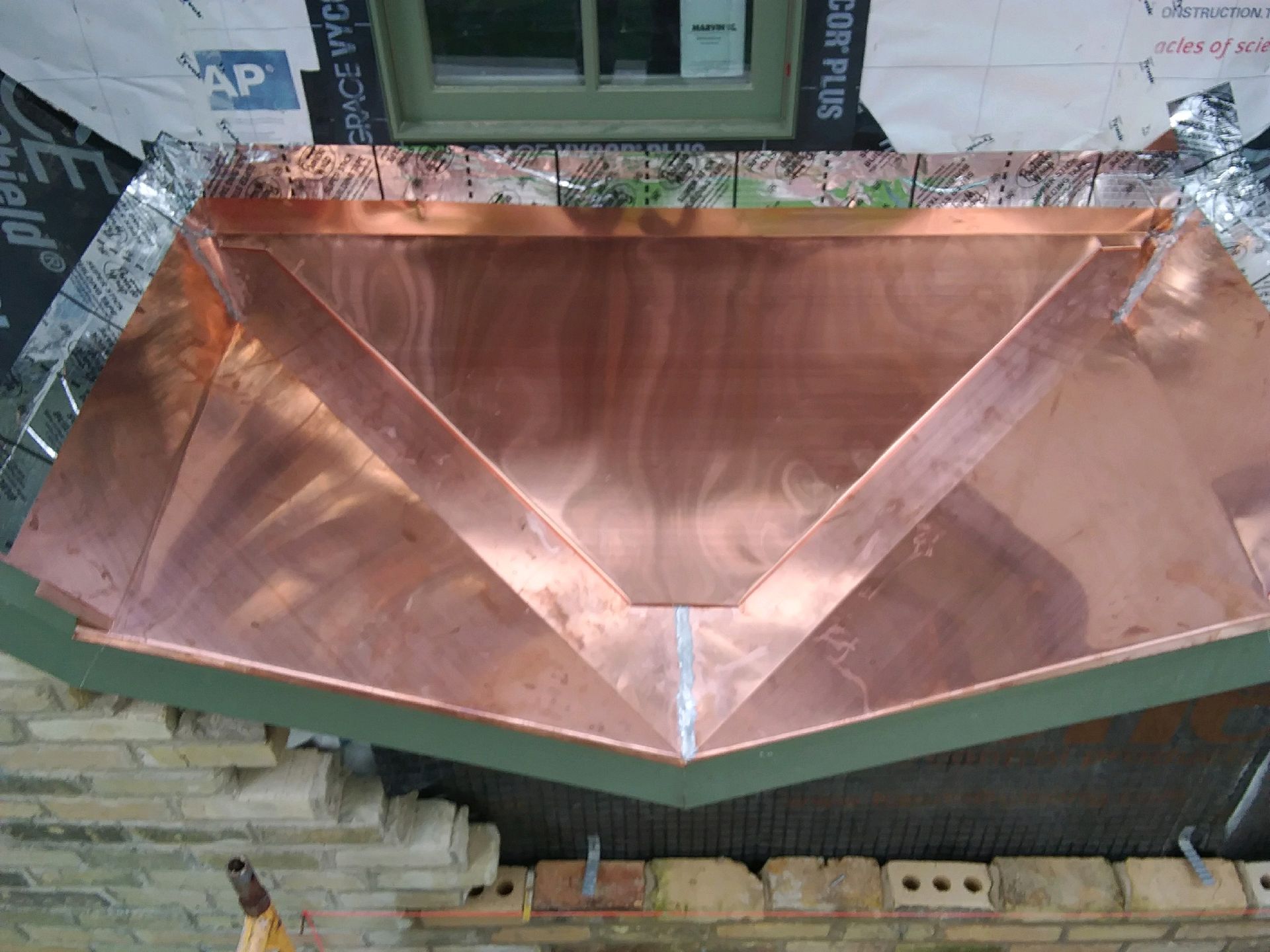 A copper canopy is being installed on a brick building