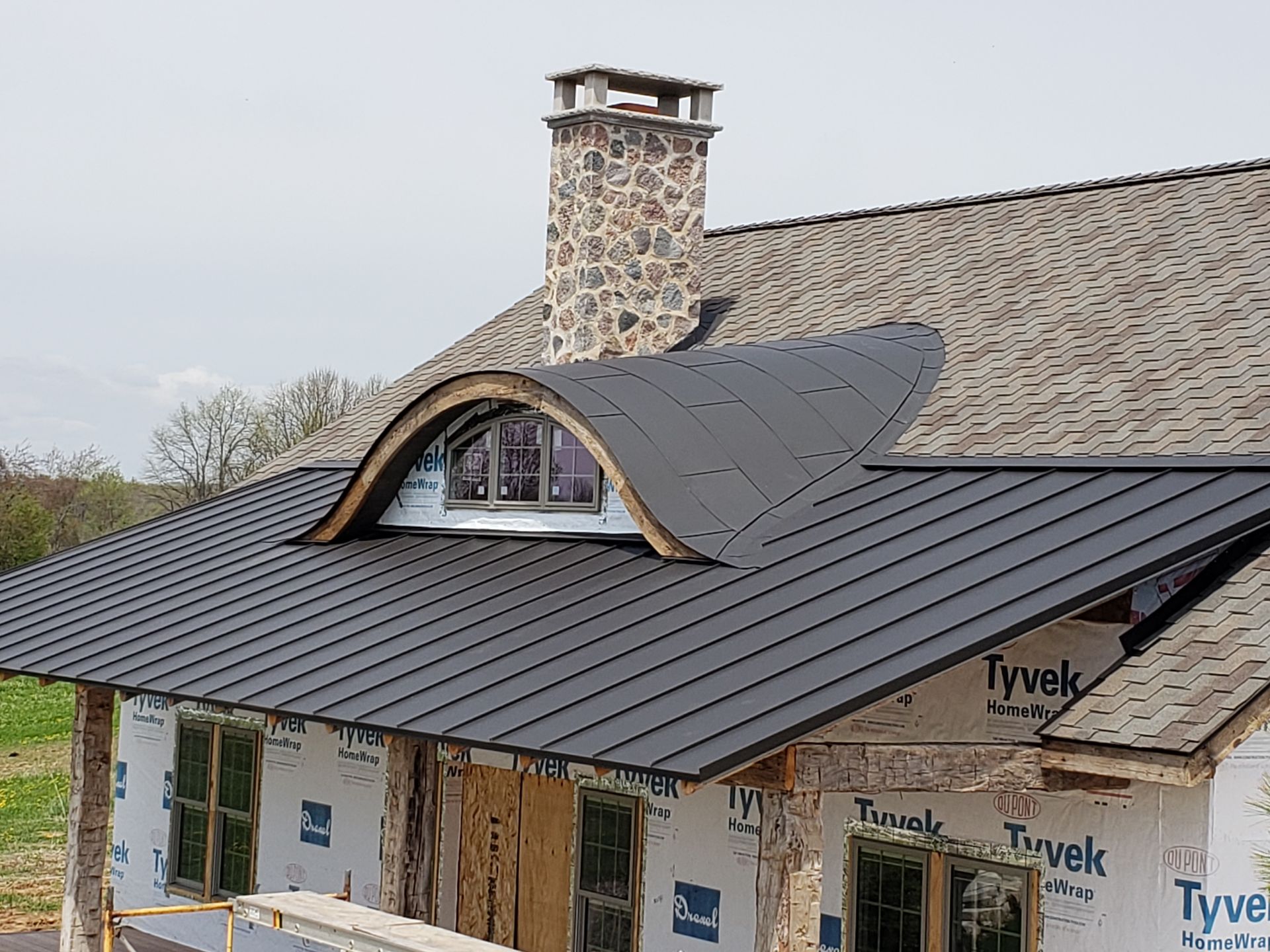 A house under construction with a black roof and a stone chimney.