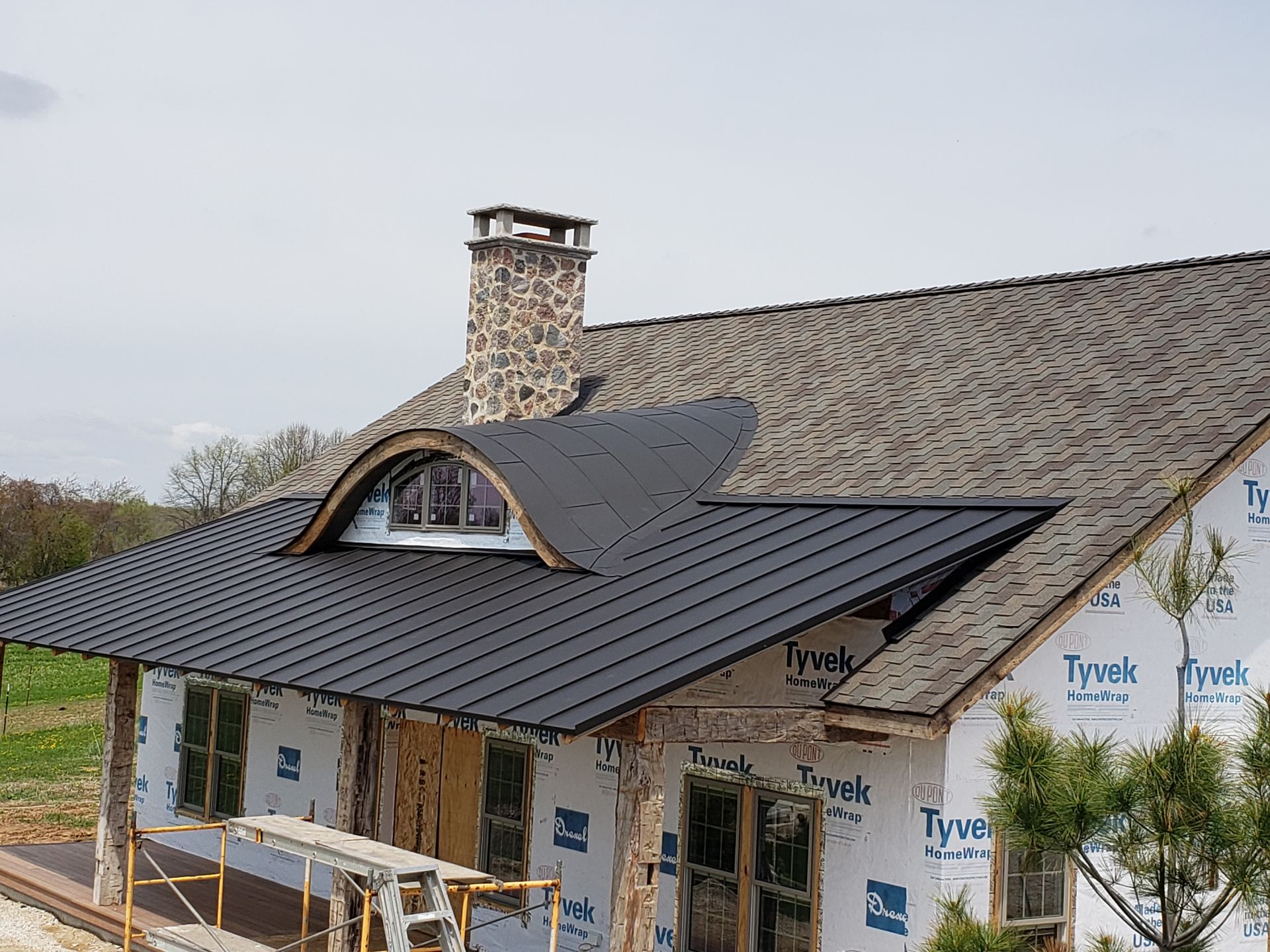 House under construction with black metal roof and stone chimney.