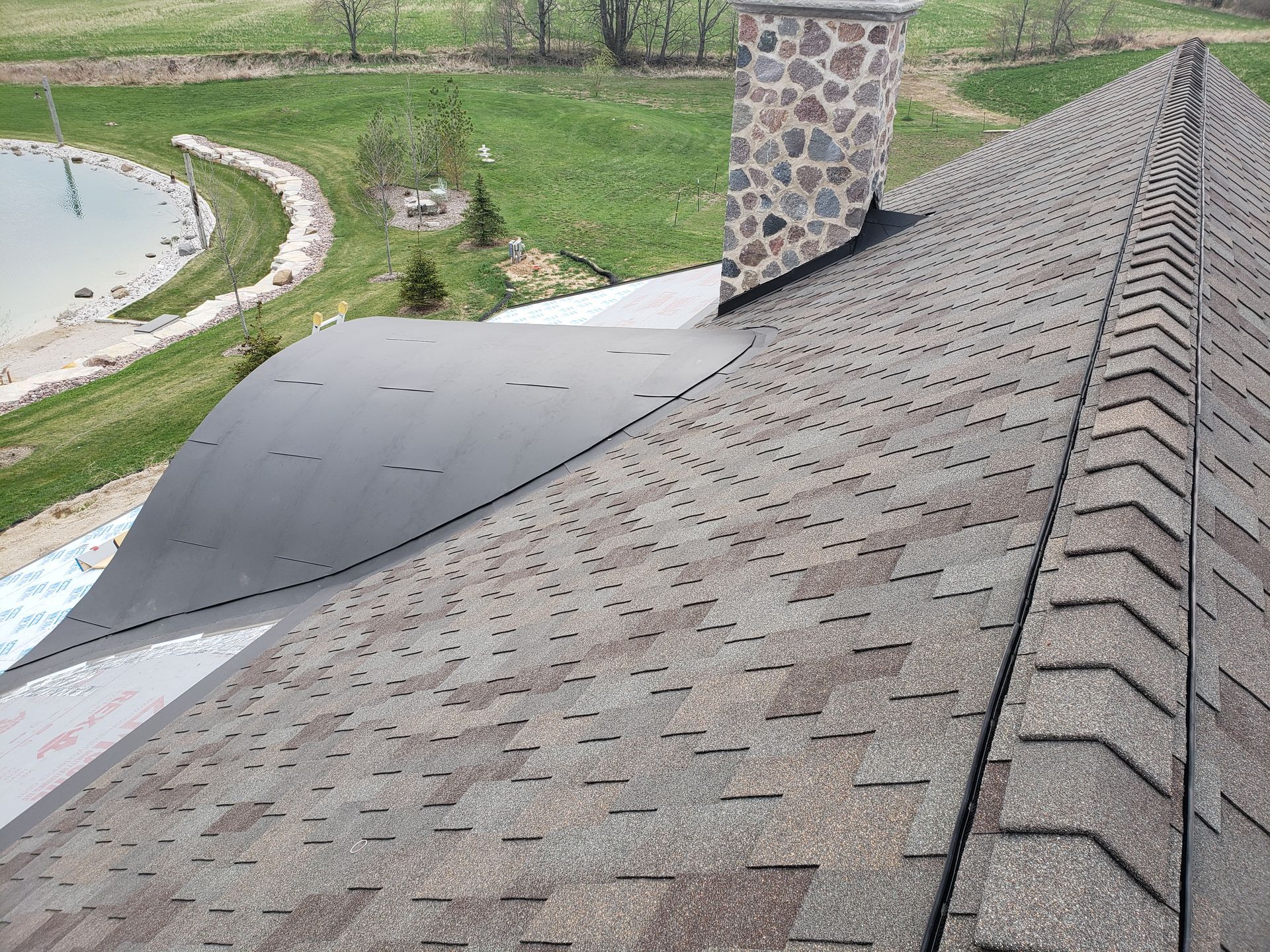 A roof with a chimney on top of it and a pond in the background.