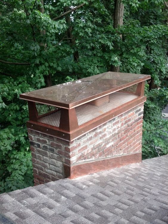 A brick chimney on top of a roof with trees in the background.