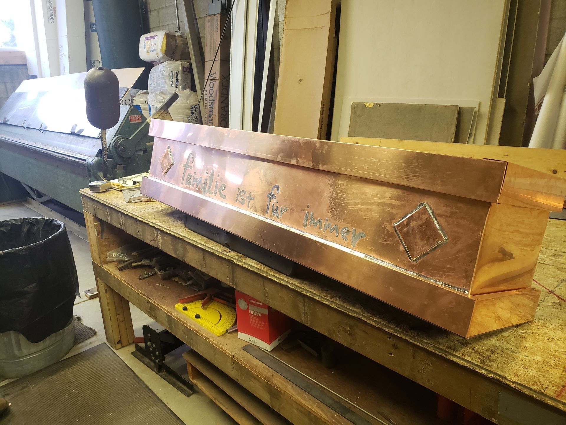 A copper coffin is sitting on a wooden table in a workshop.