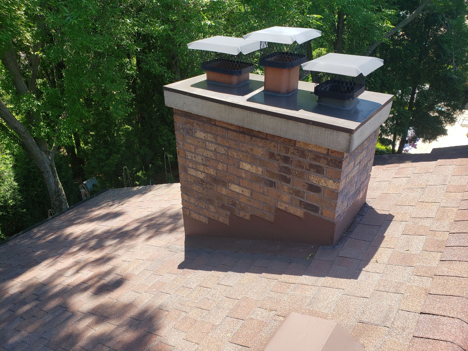 A brick chimney on top of a roof with trees in the background
