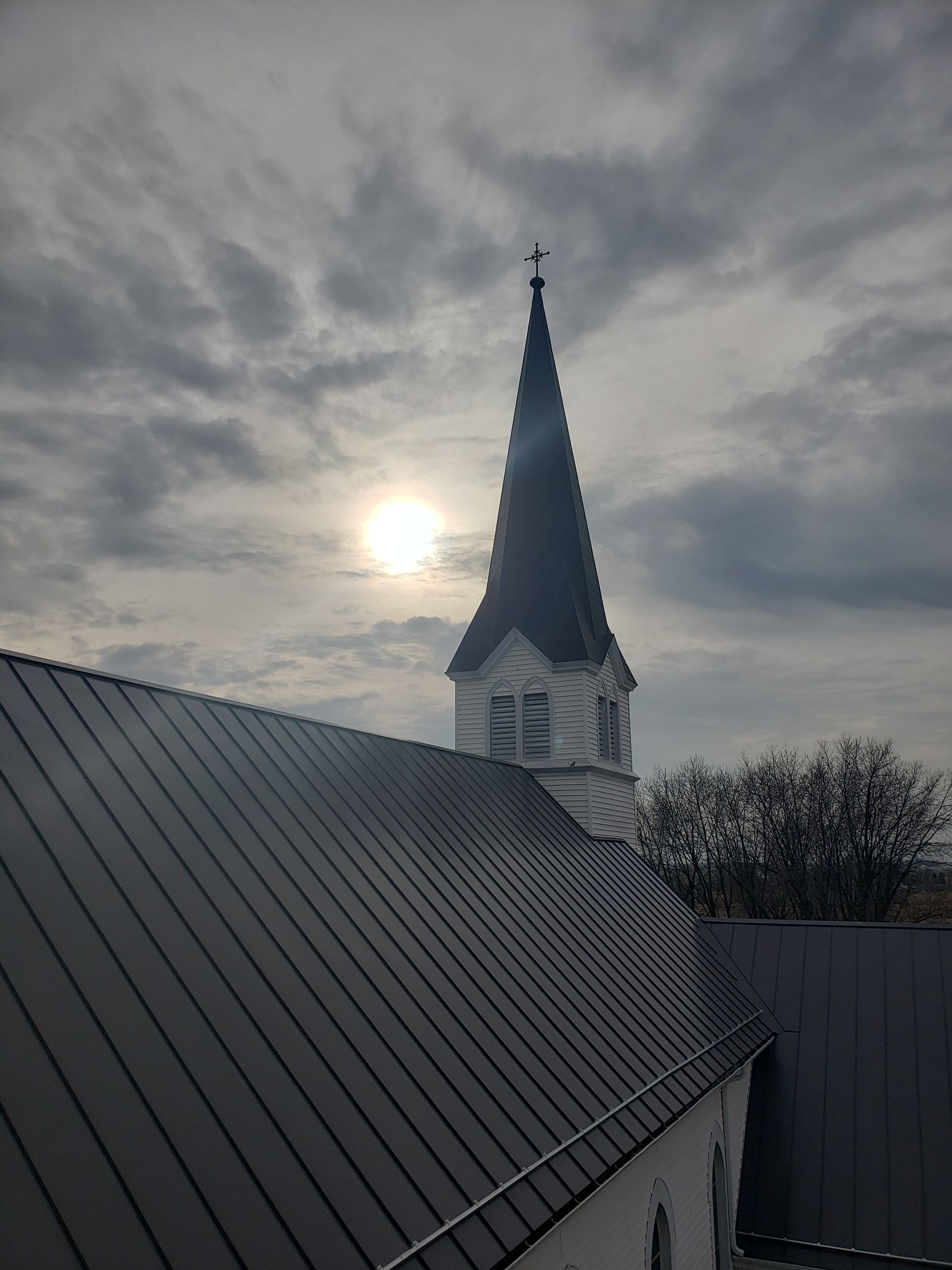 A church steeple with the sun shining through the clouds behind it.