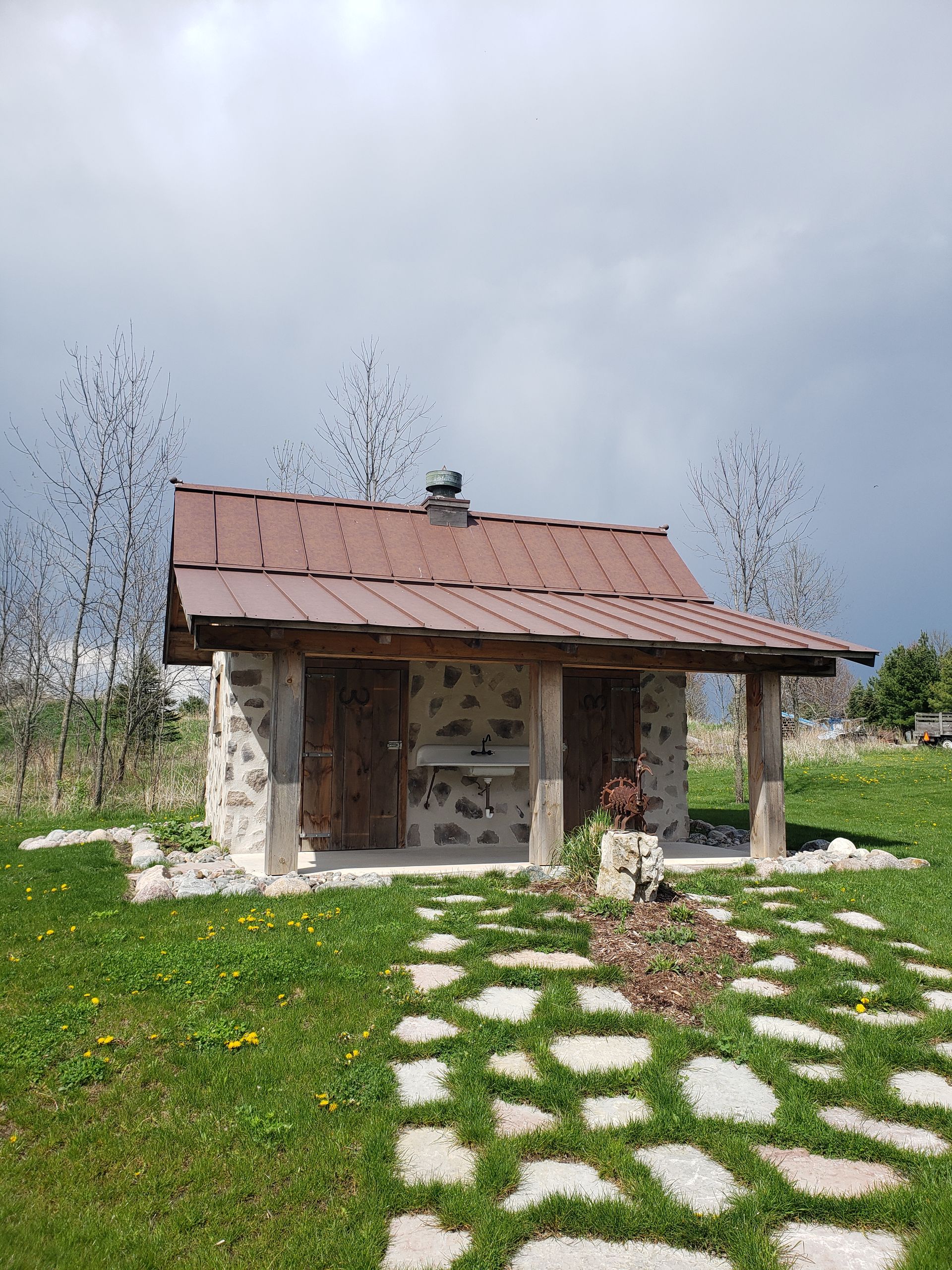 A small stone house with a metal roof is sitting in the middle of a grassy field.