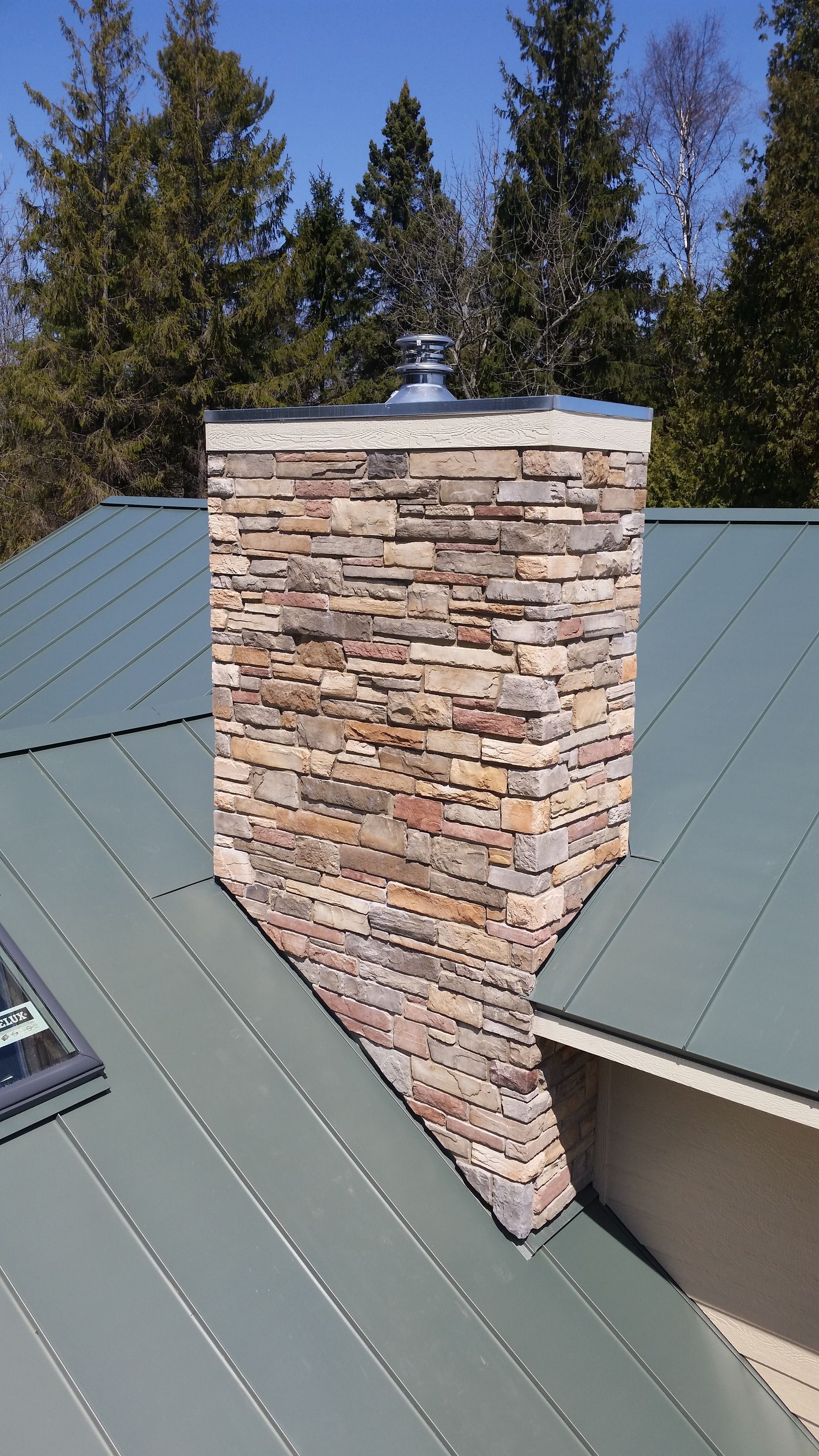 A chimney on top of a green roof with trees in the background.