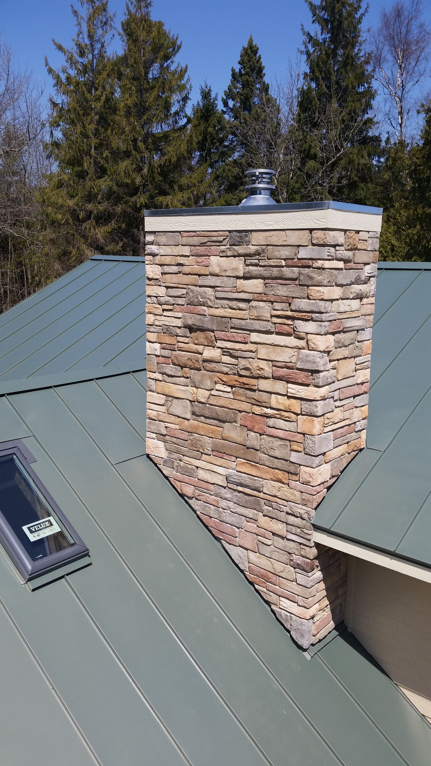 A stone chimney on top of a metal roof with a skylight.