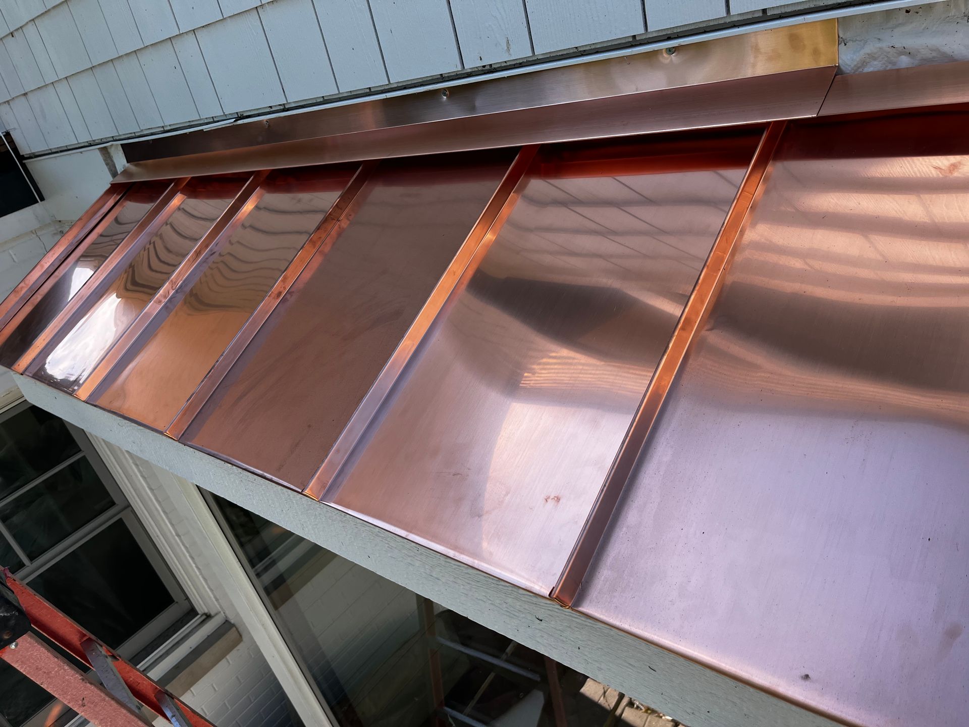 A copper canopy is being installed on the side of a building
