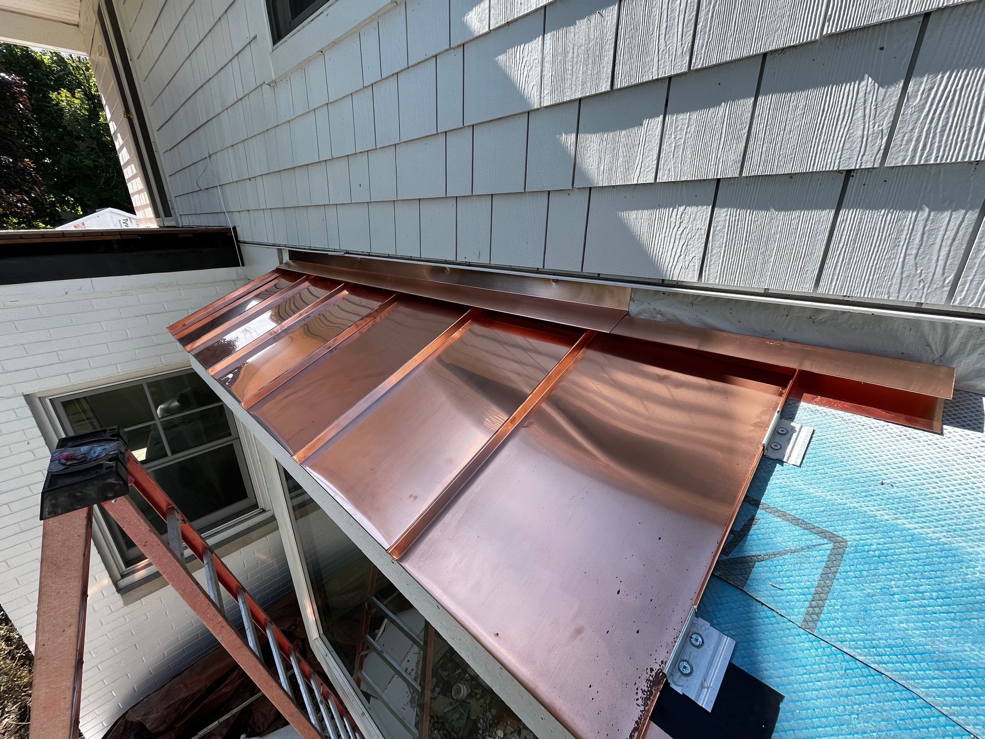 A copper roof is being installed on the side of a house