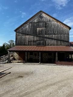 A large wooden barn with a metal roof is sitting on top of a dirt field.