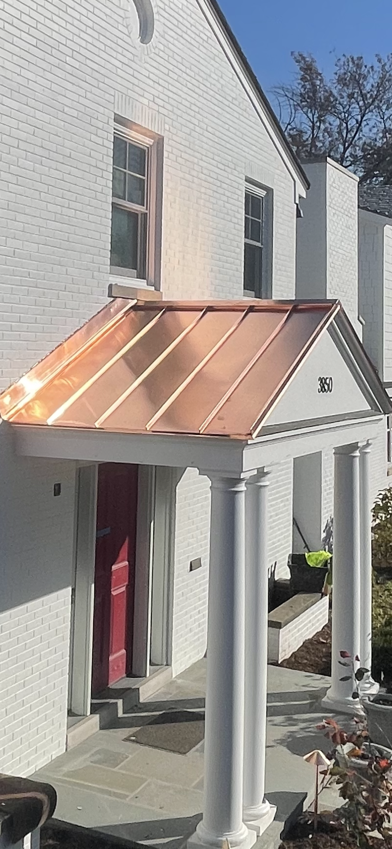 A white brick building with a copper canopy over the front door.