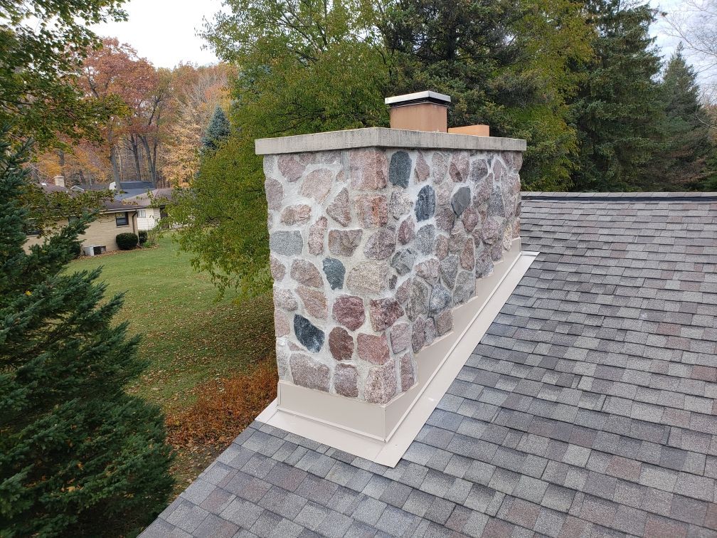 A stone chimney on top of a roof with trees in the background.
